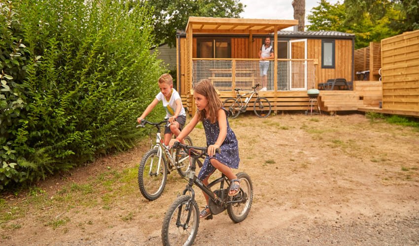 Deux enfants font du vélo à proximité de leur leur bungalow au Camping la Grande Métairie à Carnac