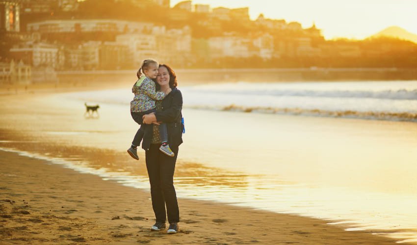 Une mère tient sa fille dans les bras sur une plage de la cote basque.