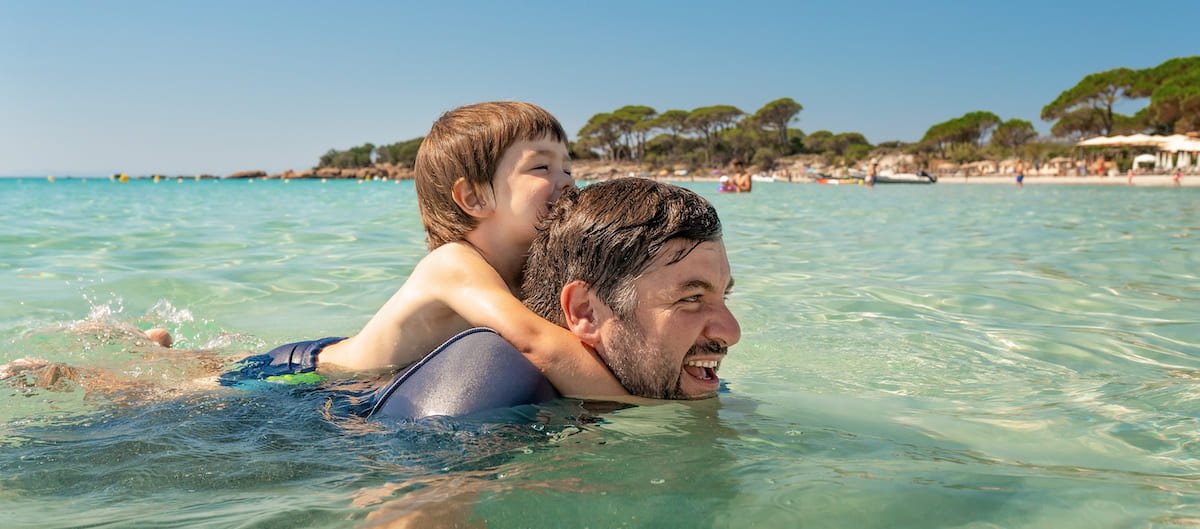 Un père et son fils se baignent sur une plage Corse lors de vacances dans un camping Tohapi.